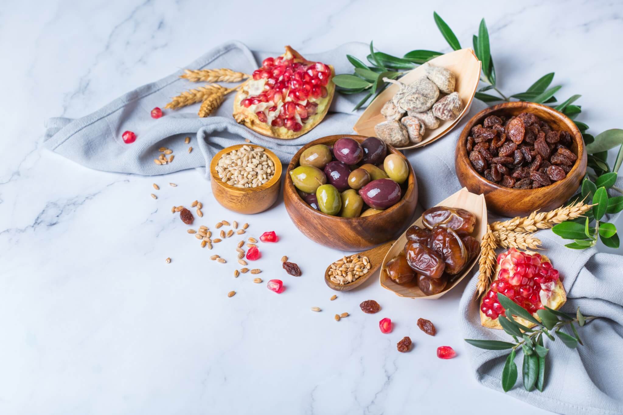 Symbols of judaic holiday Tu Bishvat, Rosh Hashana new year of the trees. Mix of dried fruits, date, fig, grape, barley, wheat, olive, pomegranate on a marble table. Copy space background